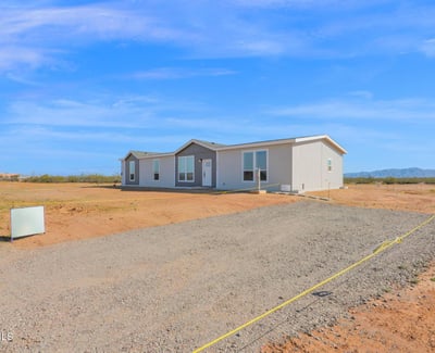 View of the home's generous acreage, gravel approach, and open desert setting. The property offers abundant space for outdoor activities, future additions, and enjoying Arizona's wide-open landscapes.