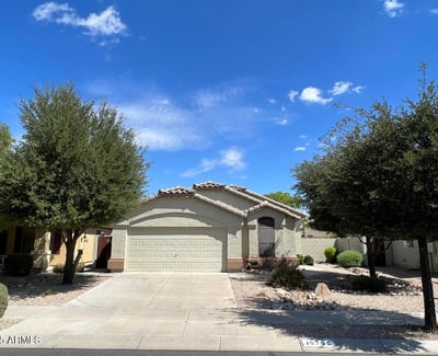 Welcoming front elevation framed by mature trees and desert landscaping for low-maintenance living. The spacious driveway and attached garage provide convenience while complementing the home's appealing design.