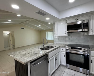 Contemporary kitchen showcasing granite counters, stainless steel appliances, abundant cabinetry, and a large peninsula overlooking the living room. The open layout creates a seamless connection between cooking, dining, and gathering spaces.