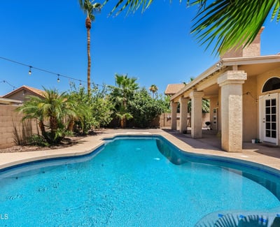 A sparkling swimming pool, mature tropical landscaping, expansive covered patio, and inviting outdoor spaces combine to create a backyard designed for year-round enjoyment in Chandler.