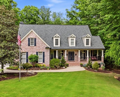 This beautiful home features a welcoming front porch, expansive lawn, and lush surrounding greenery for privacy.