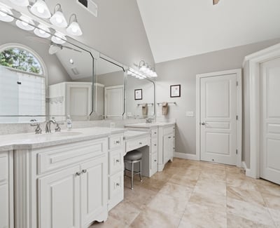Spacious bathroom featuring dual vanities, modern fixtures, and abundant natural light from an arched window.