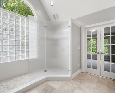 Bright and airy bathroom features a spacious glass shower and double French doors for added luxury.