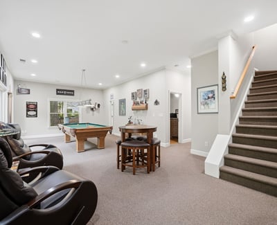 Spacious recreational area featuring a pool table, cozy seating, and an inviting staircase to the upper level.