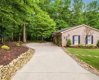 Discover a welcoming home nestled among lush greenery, featuring a spacious driveway and inviting outdoor spaces.