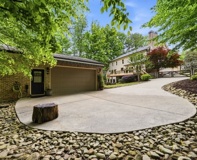 Spacious driveway with natural landscaping offers a welcoming approach to this unique property surrounded by trees.