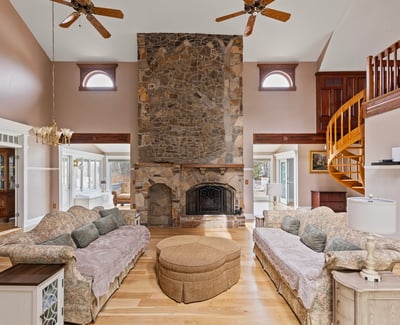 Spacious living area features a striking stone fireplace and unique spiral staircase, perfect for entertaining.
