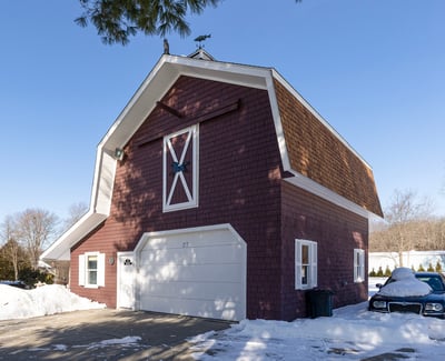 Unique barn-style home with ample space and convenient garage, set in a picturesque winter landscape.