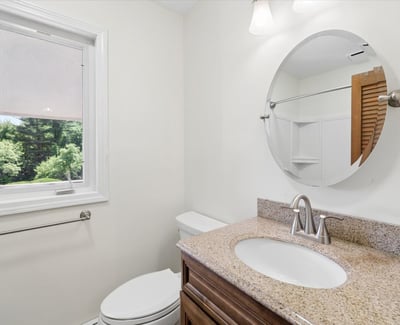 Bright bathroom featuring a circular mirror, granite countertop, and convenient window for natural light.