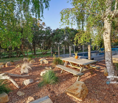 This outdoor space features a picnic area surrounded by native landscaping and a pool in the background.