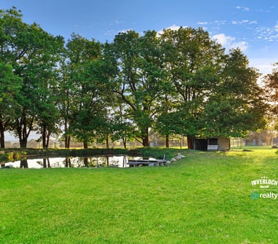 Expansive green space features a tranquil pond, surrounded by mature trees, perfect for outdoor gatherings.