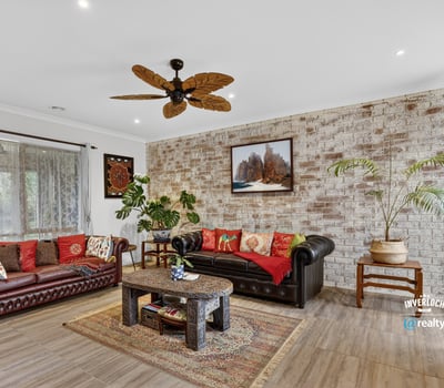 Spacious living area featuring a unique brick wall, rich colors, and a tropical-inspired ceiling fan.
