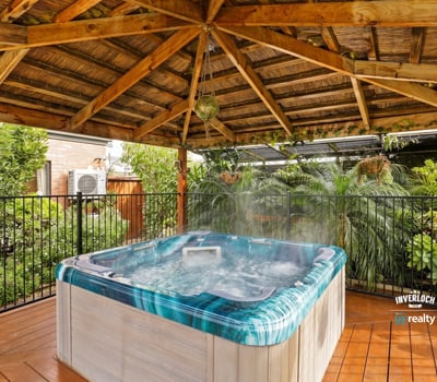 Relax in this private hot tub surrounded by lush landscaping under a rustic wooden pergola.