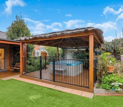 Discover a relaxing outdoor oasis featuring a covered patio and inviting hot tub surrounded by lush greenery.