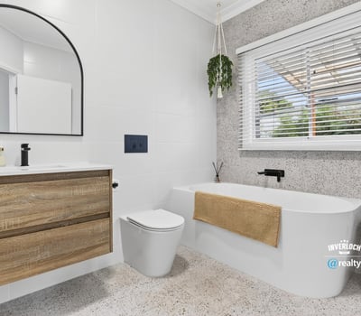 Modern bathroom featuring a freestanding tub, large mirror, and ample natural light from the window.