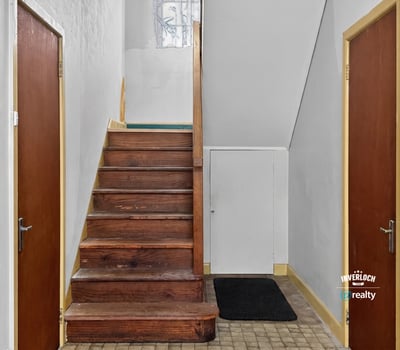 Bright entryway featuring a wooden staircase and dual access doors, perfect for welcoming guests.