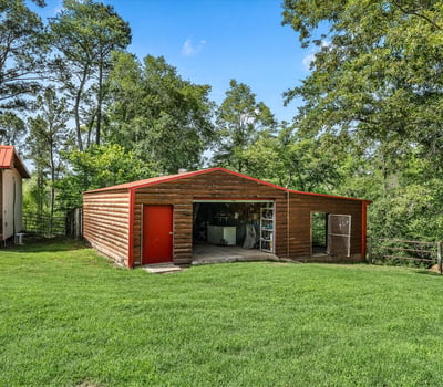 Spacious outdoor area featuring a large storage barn surrounded by lush greenery and trees.