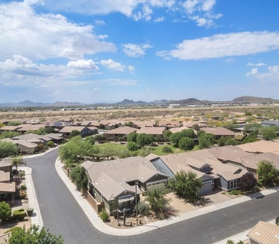 A panoramic aerial shot highlights the peaceful Phoenix neighborhood with mountain vistas, wide streets, and proximity to open desert terrain.