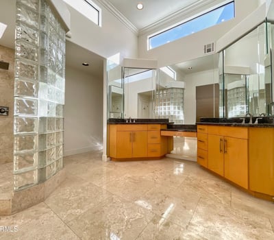 Spacious bathroom with high ceilings, glass-block shower, and granite vanities. Elegant design and natural light define this luxurious space.