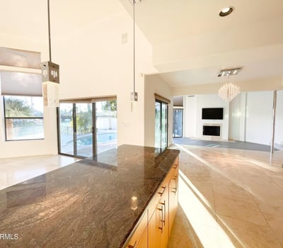 Gourmet kitchen with open flow into living area. Refined pendant fixtures and granite surfaces define this bright, upscale space.