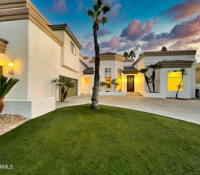The home s crisp white exterior glows against a vibrant Scottsdale sunset, surrounded by palms and a pristine front lawn.