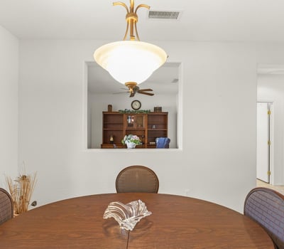 A modern dining area framed by crisp white walls and elegant lighting, offering a clear view into the private home office beyond.