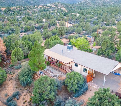 This elevated view highlights the wraparound deck, mature trees, and sprawling land. A serene retreat with endless possibilities for customization or self-sufficient living.