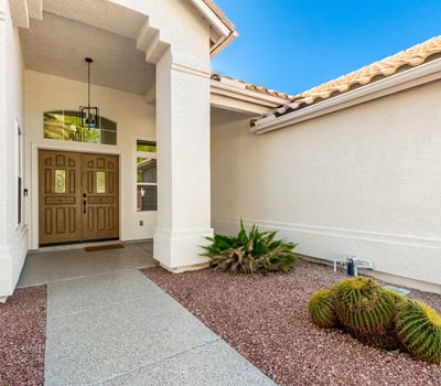 Inviting covered entry with double front doors, architectural details, and desert landscaping accents. The shaded Scottsdale entrance creates a warm and stylish arrival experience for guests and homeowners.