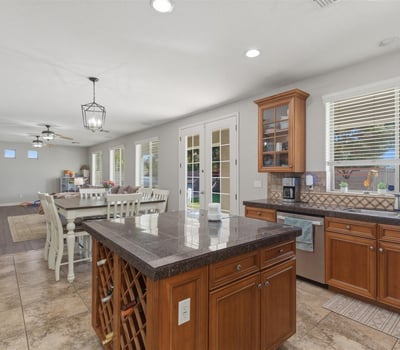 Bright kitchen with wood cabinetry, granite island, tile flooring, and large windows bringing in natural light from the backyard.