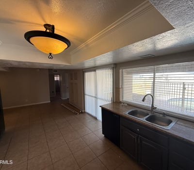 Kitchen area with double sink, tile counters, and rich cabinetry. Natural light from the wide window brightens the room while offering a glimpse of the pool area outside.