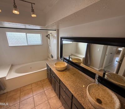Primary bathroom featuring granite countertops, dual vessel sinks, and large mirror for added functionality. Tile flooring and warm finishes create a comfortable and practical bathroom space.