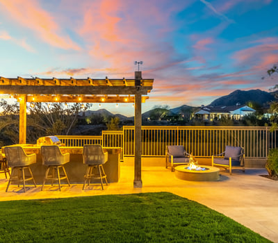 Stylish outdoor entertaining area with built-in kitchen, bar seating, and fire pit, set against scenic Scottsdale mountain views.