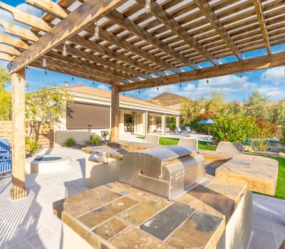 Scottsdale backyard featuring a pergola-covered outdoor kitchen with built-in grill and bar seating, ideal for entertaining guests.