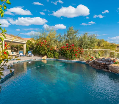 Scottsdale pool featuring a rock waterfall, lush plants, and desert landscaping, creating a peaceful outdoor setting.