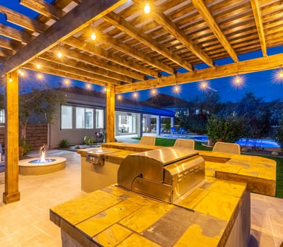 Scottsdale pergola kitchen with built-in grill, bar seating, and warm lighting, ideal for entertaining after sunset.