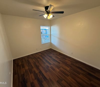 Comfortable bedroom featuring wood-look flooring, ceiling fan, and natural light. The spacious layout provides a relaxing retreat while accommodating a variety of furniture configurations.