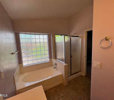 Primary bathroom designed for relaxation with a garden tub, separate shower, tile flooring, and large window. The bright and functional layout adds comfort and value to this Goodyear home.