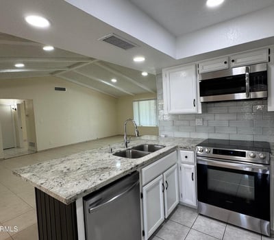 Contemporary kitchen showcasing granite counters, stainless steel appliances, abundant cabinetry, and a large peninsula overlooking the living room. The open layout creates a seamless connection between cooking, dining, and gathering spaces.