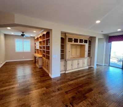Open great room with stunning custom entertainment cabinetry, built-in office shelving, upgraded wood flooring, recessed lighting, and plantation shutters creating an elegant and highly functional living space.