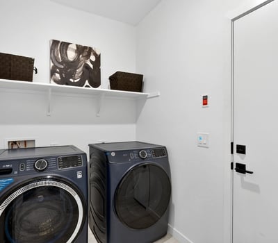 Designed for convenience, this laundry room includes upper shelving, modern appliances, and direct garage access to simplify everyday routines while maximizing storage.