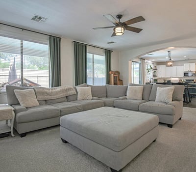 Spacious family room with plush carpeting, oversized windows, and an open layout connecting seamlessly to the kitchen. Perfect for entertaining guests or relaxing with family.