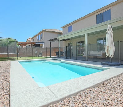 Private backyard featuring a sparkling pool, covered patio, removable pool fence, and lush lawn. A fantastic outdoor space for entertaining, relaxing, and enjoying Arizona's sunny climate.