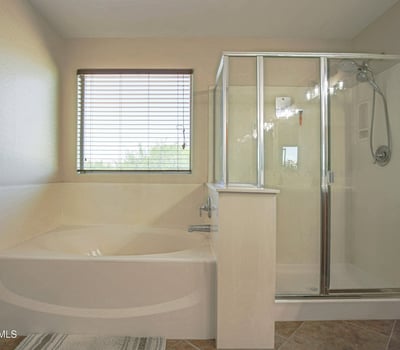 Relaxing primary bathroom featuring a deep soaking tub, separate glass shower, natural light, and spacious layout. Designed to provide both comfort and convenience in this Waddell home.