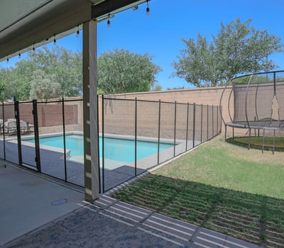 Covered patio overlooking the backyard pool, grassy area, and secure pool fencing, creating a comfortable outdoor retreat for relaxing and entertaining in this Waddell home.