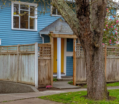 This inviting home features a unique yellow door, framed by a well-maintained wooden fence and inviting landscaping.