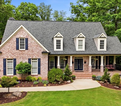 Beautiful brick home nestled in nature, featuring a spacious porch and well-maintained landscaping in a peaceful setting.