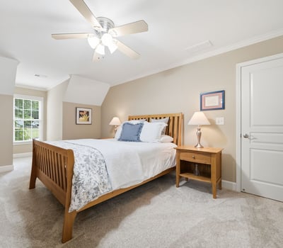Bright and inviting bedroom featuring plush carpeting, modern ceiling fan, and ample natural light.