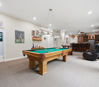 Spacious recreational room featuring a pool table and a well-equipped bar, perfect for entertaining.