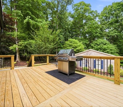 Spacious deck featuring a built-in grill, perfect for outdoor entertaining amid a lush, wooded backdrop.