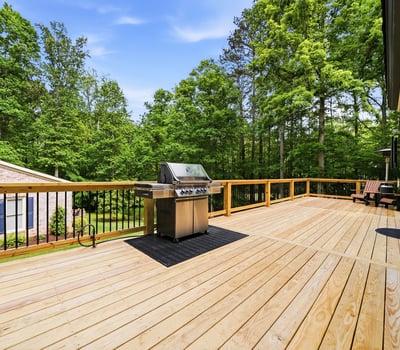 Spacious outdoor deck featuring a built-in grill, perfect for gatherings amidst lush greenery.